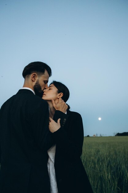 Young stylish couple of husband and wife dressed in classic suits on a photo shoot in the middle of a green field The concept of the relationship between a couple of people in love