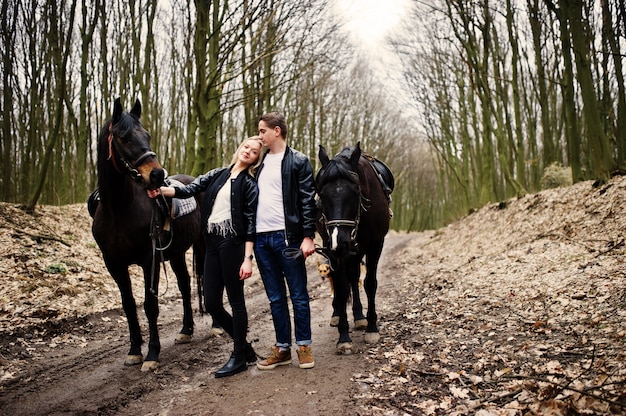 Giovani coppie alla moda nell'amore vicino ai cavalli alla foresta di autunno