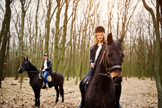 Young stylish couple riding on horses at autumn forest 