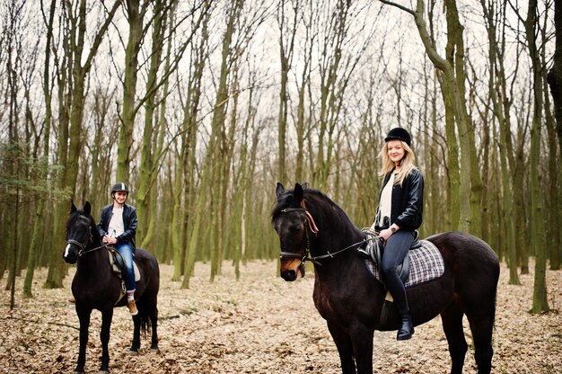 Young stylish couple riding on horses at autumn forest 