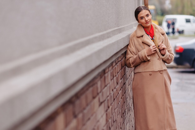 Young stylish cute girl in a fur coat strolling around the city near wooden houses and stone walls