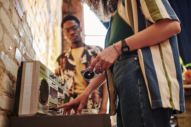 Photo young stylish female putting cassette with her favorite music into stereo player