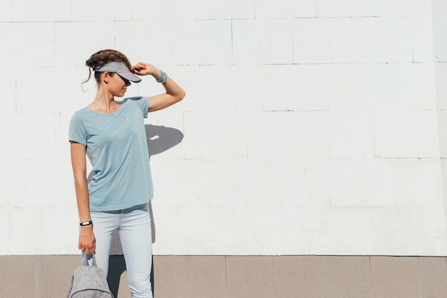 Young stylish girl in a cap on a white wall