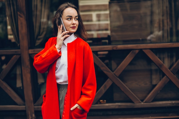 Foto giovane ragazza alla moda in un cappotto rosso in piedi in una città d'autunno