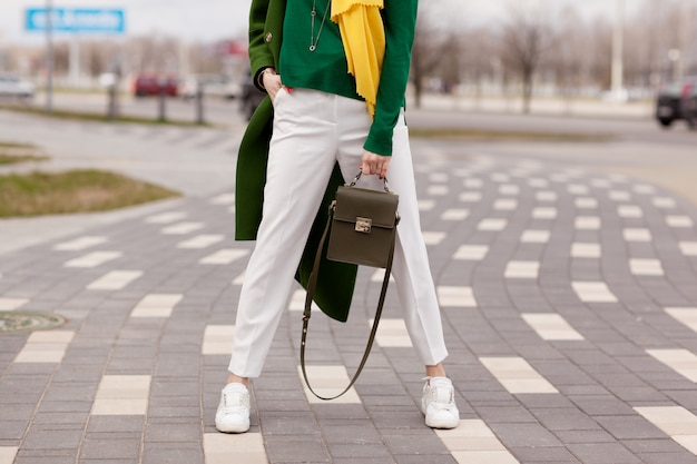 Ragazza giovane ed elegante in pantaloni bianchi, cappotto verde caldo