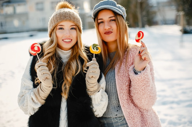 Ragazze giovani e alla moda in abiti invernali stanno camminando nel parco solare con i dolci