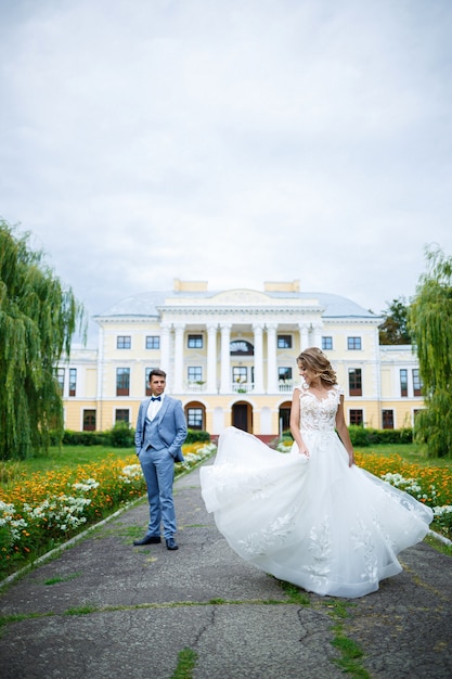 Young stylish guy in the costume of the groom and the bride beautiful girl in a white dress with a train walk in the park on their wedding day