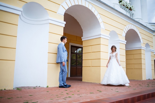 新郎と新婦の衣装を着た若いスタイリッシュな男と白いドレスを着た美しい少女が結婚式の日に公園を散歩します