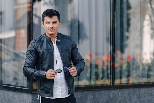 Young stylish guy in glasses in black leather jacket on glass background