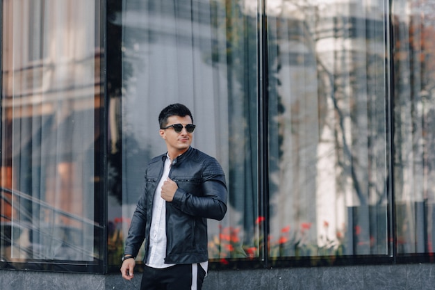 Young stylish guy in glasses in black leather jacket on glass 