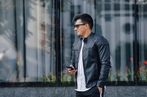 Young stylish guy in glasses in black leather jacket with phone 