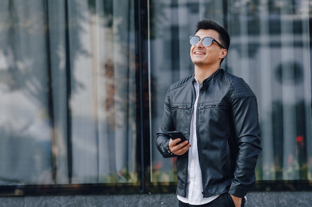 Young stylish guy in glasses in black leather jacket with phone 