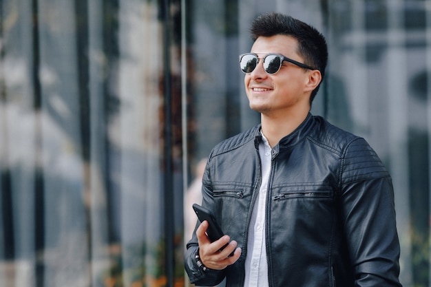 Young stylish guy in glasses in black leather jacket with phone 