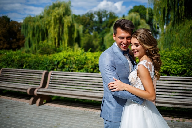 Foto giovane ragazzo alla moda in un vestito lo sposo e la sposa bella ragazza in un vestito bianco con un treno a piedi nel parco il giorno delle nozze