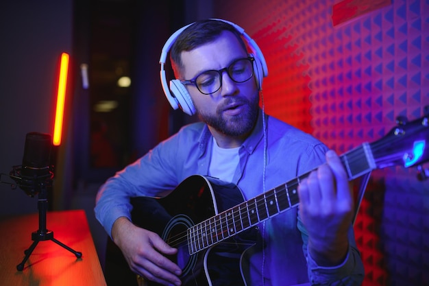 A young stylish guy with a beard wearing casual or music teacher playing guitar in front of smartphone camera Online guitar training or vocal lesson