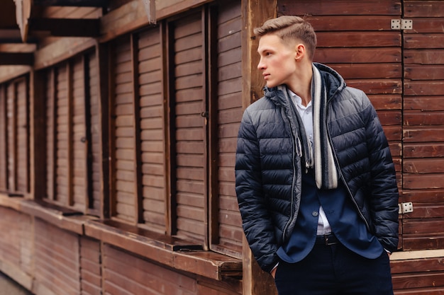 Young stylish guy with a monumental face walks in a cool city near the wooden and stone walls