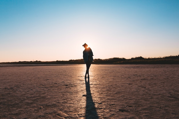 Photo young stylish hipster girl silhouette jeans jacket sunset coast during travel summer holidays vacation outdoors