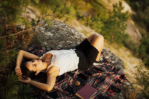 Young stylish hipster woman lying on the rock on the mountain.