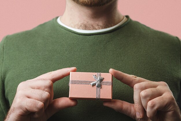 Un giovane uomo elegante detiene una bella scatola rosa con un regalo per san valentino