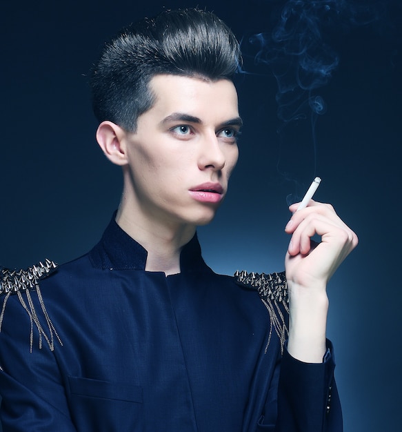 Молодой стильный человек курит сигарету. Студийный снимок.