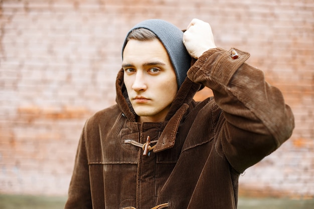 Young stylish man wears a hood on a of red brick wall