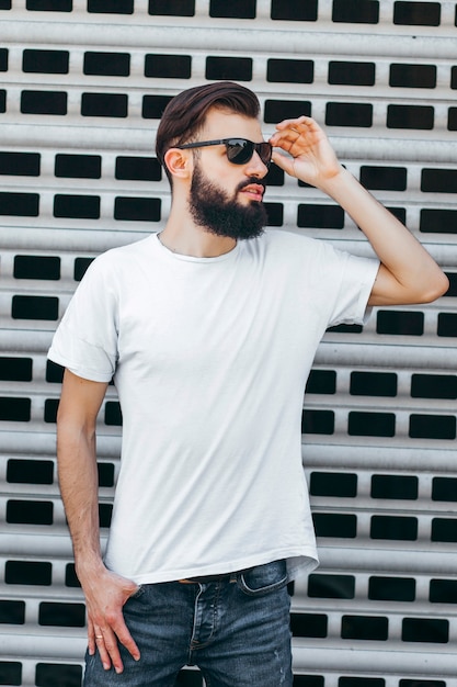 Молодой стильный мужчина с бородой в белой футболке и очках Уличное фото