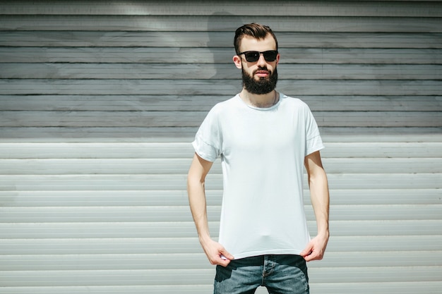 A young stylish man with a beard in a white Tshirt and glasses