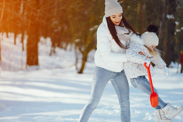 young and stylish mom playing with her little cute daughter in winter snow park 