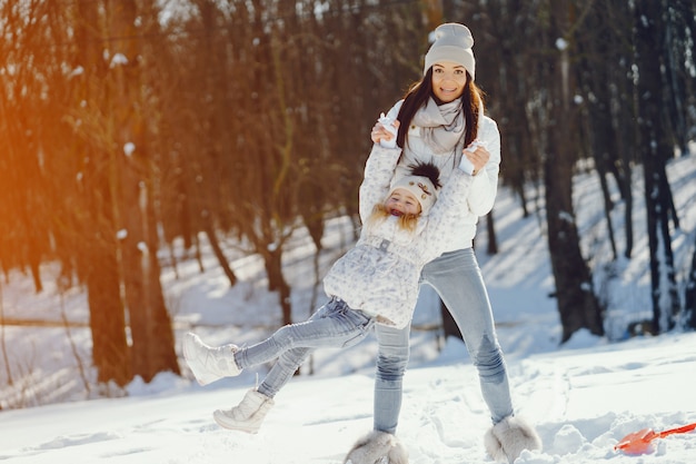 Mamma giovane e alla moda che gioca con la sua piccola figlia carina nel parco di neve invernale