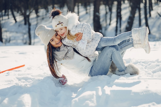 young and stylish mom playing with her little cute daughter in winter snow park 