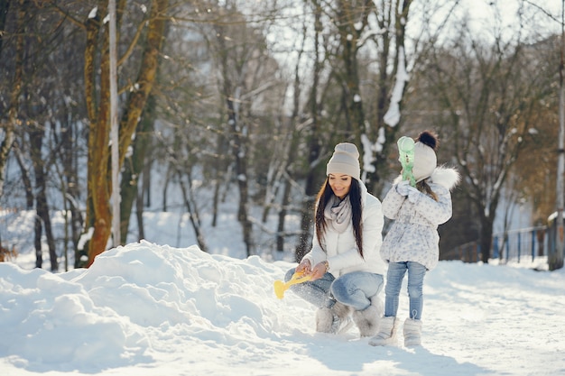 彼女の小さなかわいい娘と冬の雪の公園で遊ぶ若くてスタイリッシュなママ