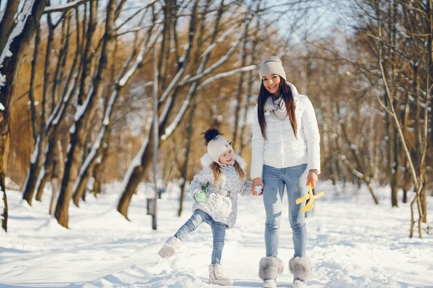 young and stylish mom playing with her little cute daughter in winter snow park 