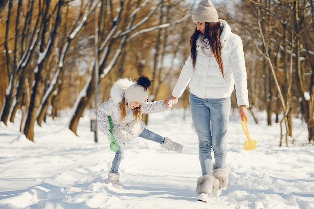 young and stylish mom playing with her little cute daughter in winter snow park 