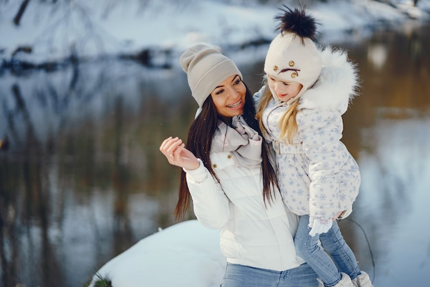 Mamma giovane e alla moda che gioca con la sua piccola figlia carina nel parco di neve invernale