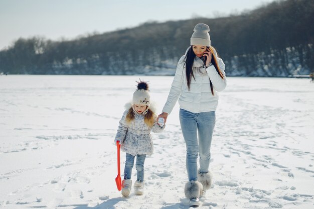 молодая и стильная мама, играющая с ее маленькой милой дочерью в зимнем снежном парке