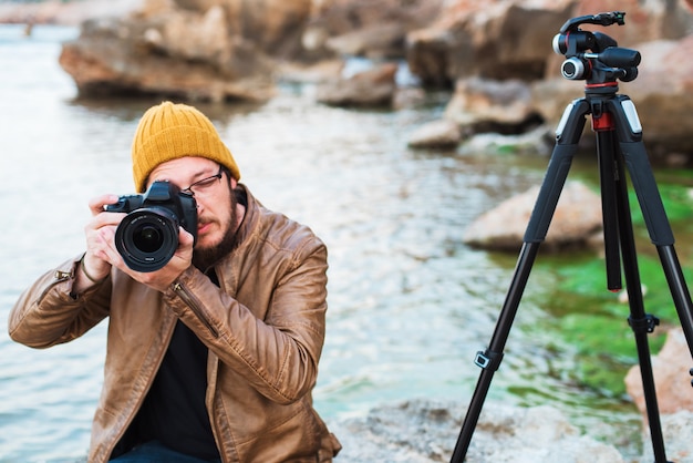 Young stylish photographer sitting on rock and making photo of you