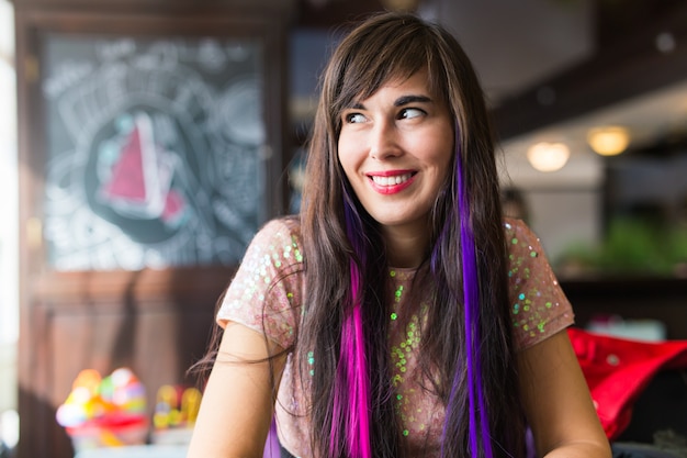 Young stylish trendy woman with multi-coloured strand in hair sits in cafe