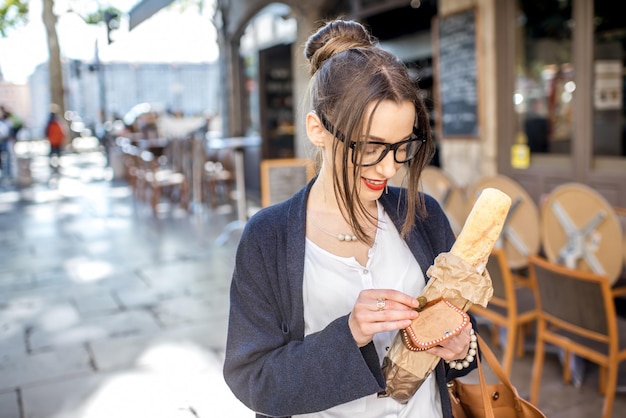 Giovane donna alla moda che compra una baguette francese che sta sulla via nella città di lione