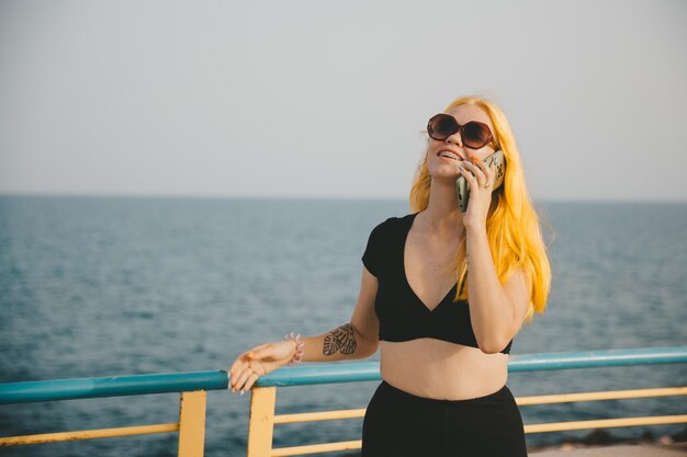 A young stylish woman communicates on a smartphone on the city\
embankment rest and work in nature by the sea