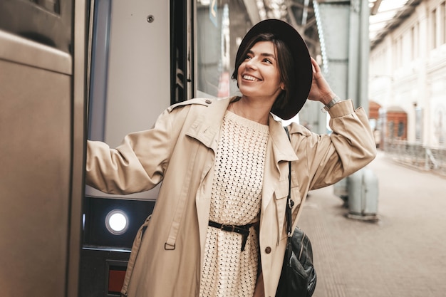 Young stylish woman hanging and smiling on the platform of a train carriage.