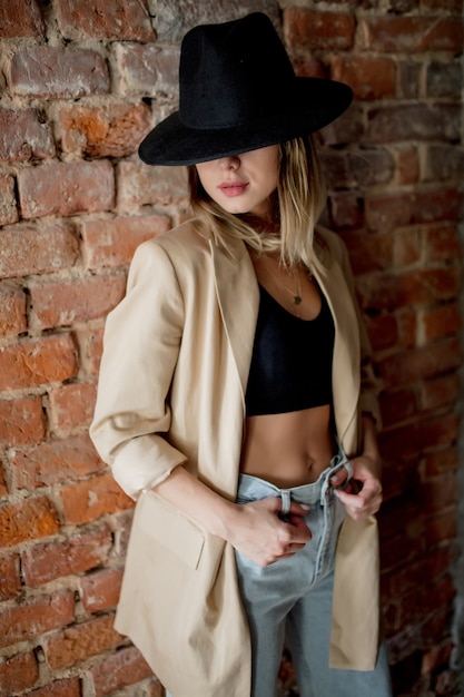 Young stylish woman in hat and clothes on a brick wall wall