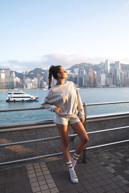 La giovane donna alla moda sta proponendo nel porto di victoria, città di hong kong.