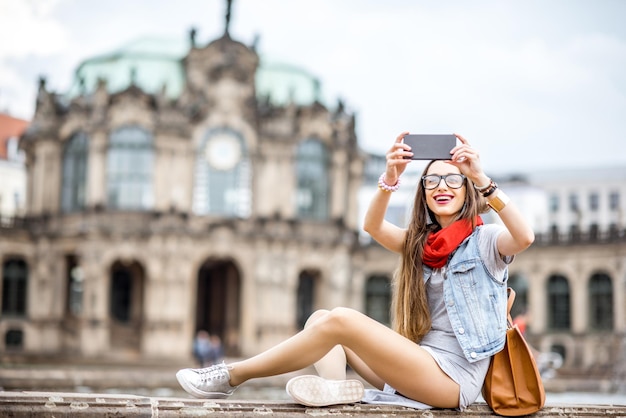 Young stylish woman photographing with phone the old town of Dresden ciy, Germany