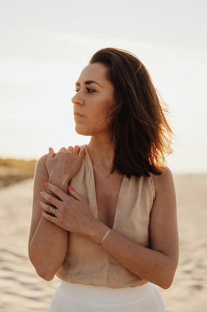 Young stylish woman poses on the beach at sunset