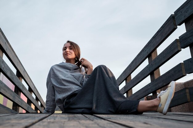 Young stylish woman resting on the bridge Attractive girl with long hair sitting on wooden floor outside