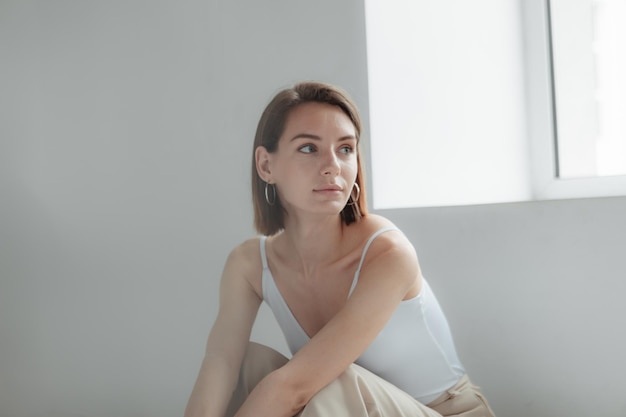 Young stylish woman sitting by a light window in a white room