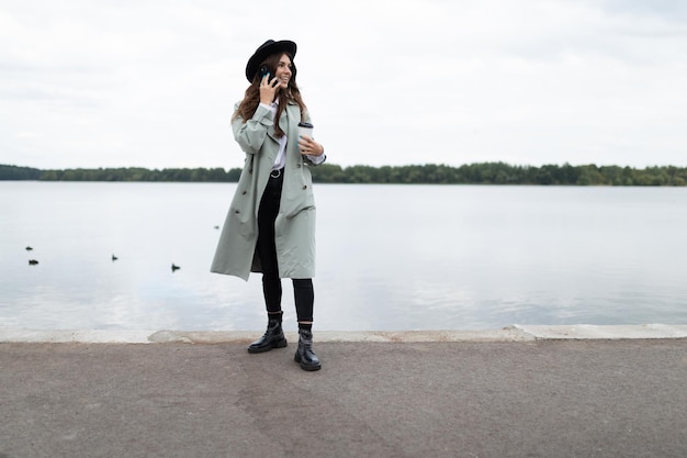 Young stylish woman speaks on a mobile phone on the embankment against the background of the sea