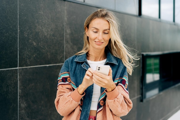 Photo young stylish woman using phone for online messages while standing outside