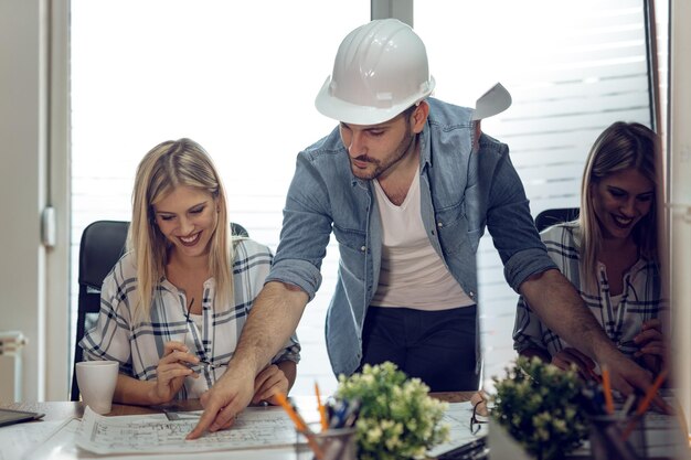 Foto giovani colleghi architetti di successo che parlano e analizzano i progetti mentre lavorano a un nuovo progetto in ufficio.