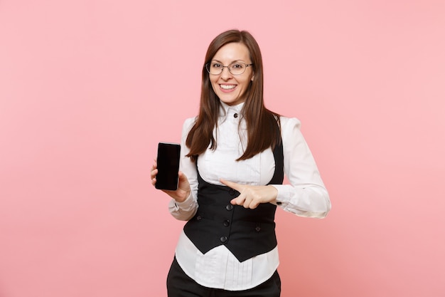 Young successful business woman holding pointing index finger on mobile phone with blank empty screen isolated on pink background. Lady boss. Achievement career wealth. Copy space for advertisement.